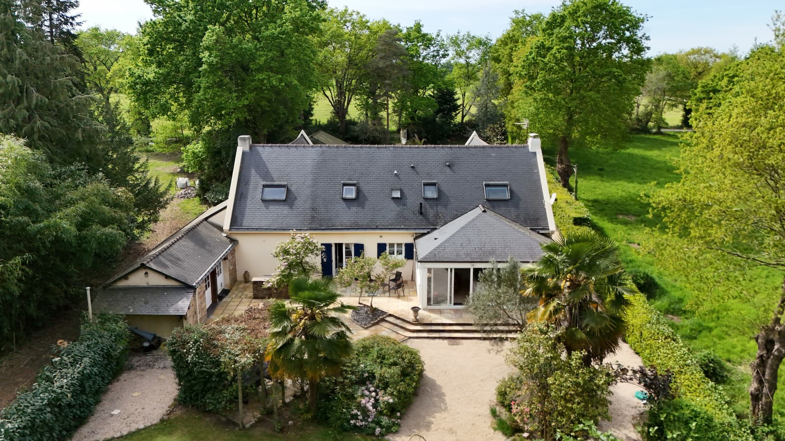 Photo drone d'un pignon de maison avec volets bleus, palmier et salon de jardin